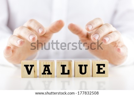 Conceptual image of a businessman in shirtsleeves holding his hands protectively above a line of wooden cubes with the word - Value.