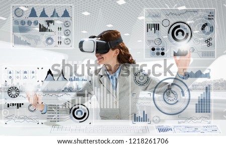Conceptual image of confident young business woman in suit using virtual reality headset and digital media interface while sitting inside bright office building.