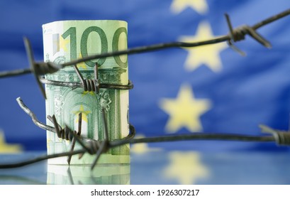 Conceptual Image Of European Union Currency Wrapped In Barbed Wire Against Flag Of EU As Symbol Of Economic Warfare, Sanctions And Embargo Busting.