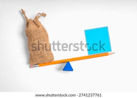 Conceptual image of financial imbalance using a sack and paper card on a pencil balance beam, representing deficit, unequal distribution, cost burden, revenue shortfall, or economic instability.