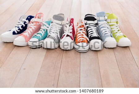 Conceptual image of gumshoes sneakers shoes on vintage wood floor in different sizes, lifestyle concept.


