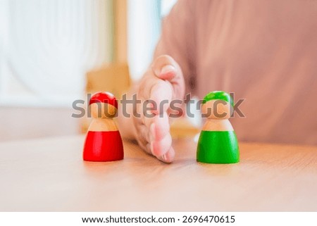 Conceptual image of a hand placed between a red and green wooden figure, showing bias or favoritism towards the green side, symbolizing decision-making, discrimination, or preference.