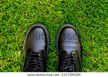 Conceptual image of legs and feet in stylish leather boots on green grass in spring and summer. Feet shoes walking in nature. Feet walking on foliage Outdoor.