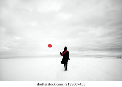 Conceptual Image Of A Lonely Young Woman With A Red Balloon In The Middle Of A White Snowy Field