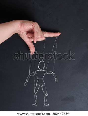 Conceptual image of manipulation, a human hand holding strings leading to a chalk-drawn puppet mannequin on a blackboard.