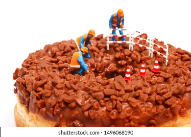 Conceptual Image Of A Miniature Figure Workmen Stood On A Chocolate Doughnut Looking Down The Centre Hole