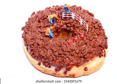 Conceptual Image Of A Miniature Figure Workmen Stood On A Chocolate Doughnut Looking Down The Centre Hole