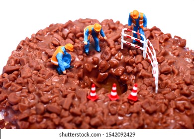 Conceptual Image Of A Miniature Figure Workmen Stood On A Chocolate Doughnut Looking Down The Centre Hole