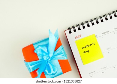 Conceptual image of mother's day in the month of May. Greeting on yellow sticky note on calendar over white. Besides  red-wrapped gift tied with blue ribbon. Focus on sticky note. - Powered by Shutterstock