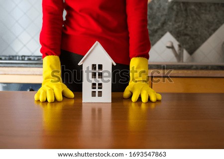 Conceptual image of person with kitchen gloves and a model house over a table