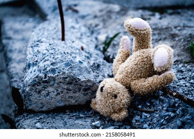 Conceptual image: Russia's war against Ukraine. Children's toy teddy bear lies on broken construction  debris against the background of destroyed building.