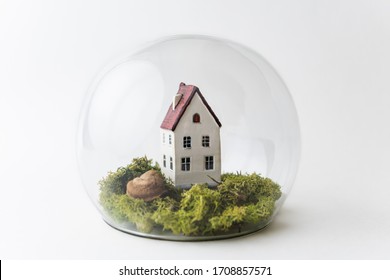 Conceptual image of safety when staying at home during Corona virus COVID-19 quarantine lockdown. Small toy house under the glass with moss and grass around.