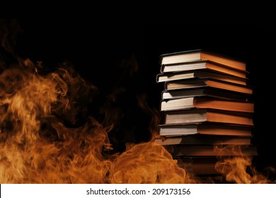Conceptual image of a tall stack of hardcover books in a burning fire with flames and smoke swirling around them in a darkened room with copyspace