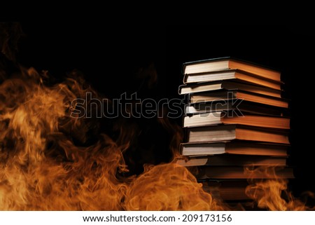 Conceptual image of a tall stack of hardcover books in a burning fire with flames and smoke swirling around them in a darkened room with copyspace