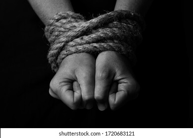 Conceptual monochrome image of woman hands tied with a coarse rope and selective lighting