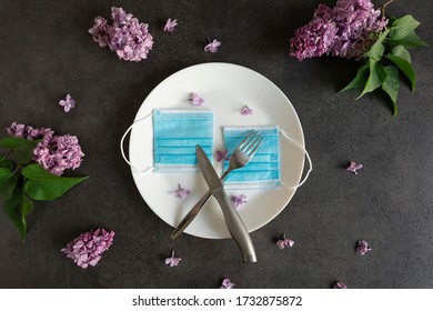 Conceptual Photo About The Long-awaited Opening Of Restaurants After Quarantine. Plate, Cutlery, Medical Mask On A Table Decorated With Spring Flowers As A Symbol Of The End Of Social Isolation.