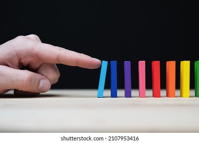 Conceptual photo of a hand starting a chain reaction with colored dominoes.
Domino effect with colored stones and copyspace. 