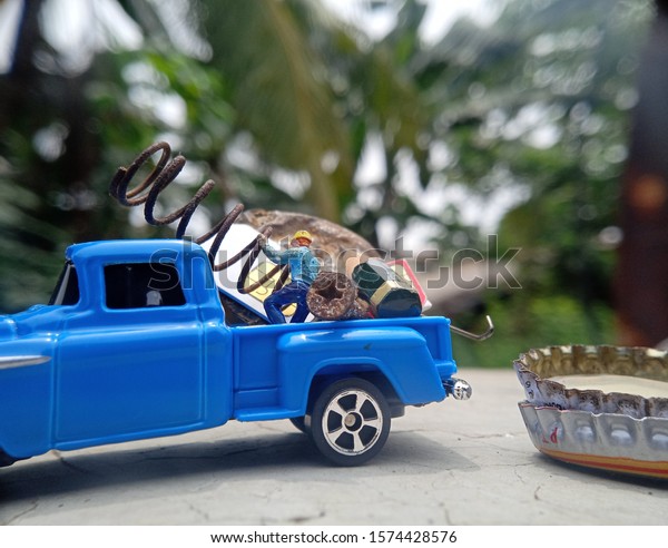 Conceptual Photo, Mini Figure Scavenger worker Loading\
corrosive bottle cup, screw, pencil, SIM card, spring and other\
used good into blue car\
\
