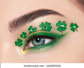 Conceptual photo of St. Patrick's Day. The eye of the young beautiful woman with bright green shadows and expressive eyebrows. Shamrock patterns. Holiday makeup - Powered by Shutterstock