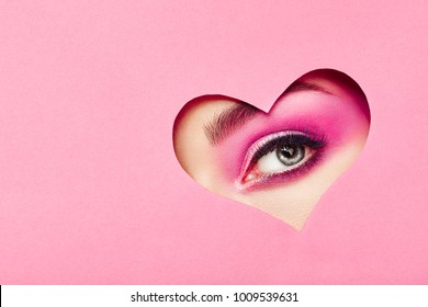 Conceptual photo of Valentine's day. Eye of Girl with Festive Pink Makeup. Paper heart on a pink background. Love symbols Valentines day - Powered by Shutterstock