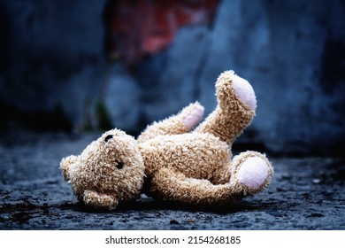 Conceptual photography: war, death and lost childhood. Conceptual picture of a children's toy teddy bear on a background of broken concrete wall.