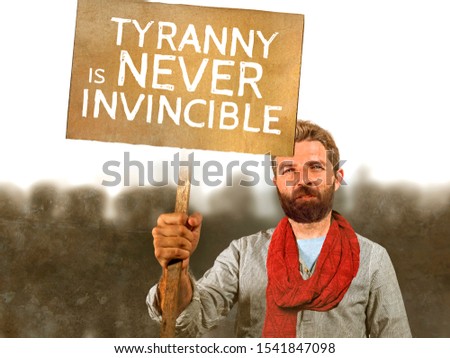 conceptual portrait of attractive hipster with scarf and beard protesting at political demonstration holding billboard with the message tyranny is never invincible defending human rights 