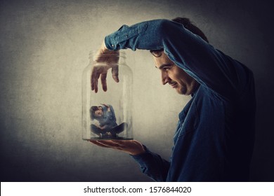 Conceptual Scene, Scared Tiny Boy Trapped Inside A Glass Jar Held In Hand By A Scary Giant. Surreal Nightmare, Child Adoption Through The Eyes Of A Teen. Helpless Captive Kid Victim Of Family Abuse.