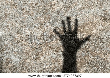 Conceptual shadow of an open human hand palm on a gray textured cement wall.