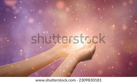Conceptual Visualization Of Male Or Female Hands Reaching Out In Prayer On Magical Dark Purple Background. Person Connecting With Higher Spiritual Energy Through Bright Light In Their Palms.