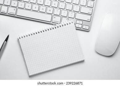 Conceptual White Ballpoint Pen, Clean Spiral Notes, Computer Keyboard And Mouse On Top Of White Table With Copy Space At The Center.