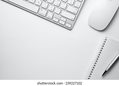 Conceptual White Ballpoint Pen, Clean Spiral Notes, Computer Keyboard And Mouse On Top Of White Table With Copy Space At The Center.