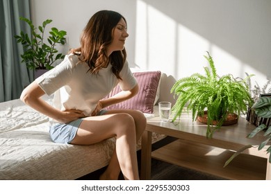 Conceptual of woman suffering menstrual pain, period cramp. Young woman holding belly sitting in bed suffering from pain during menstruation.