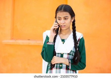 Concern Indian Young Girl talking on Smart phone, Female kid with sad Expression holding Android Cellphone against orange background. Examination result.copy space - Powered by Shutterstock