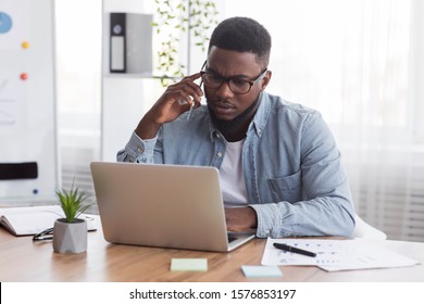 Concerned African American Employee Talking On Mobile Phone And Looking At Laptop Screen, Having Issues With Project, Copy Space