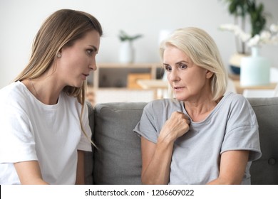 Concerned aged mother and adult daughter sit on couch having serious conversation, young woman talk with worried elderly mom, listen to her sharing problems or concerns, help dealing with depression