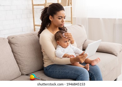 Concerned Black Mother With Sick Baby Using Tablet Video Calling Doctor Having Medical Consultation Online Sitting On Couch At Home. Mom Browsing Internet Touching Ill Child's Forehead Indoors