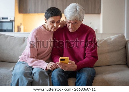 Concerned elderly couple checking smartphone on couch. Seniors read suspicious message, husband wife phone scam victim, online fraud, stress from message, risk digital security concerns for seniors