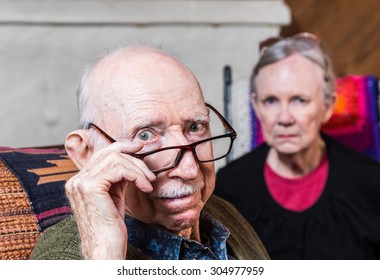 Concerned elderly couple sitting in livingroom scowling