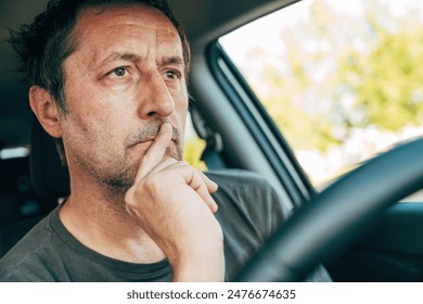 Concerned male driver thinking with index finger on lips while driving a car, selective focus - Powered by Shutterstock