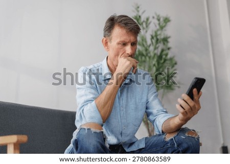 Concerned man reading message on mobile phone, experiencing stress and apprehension