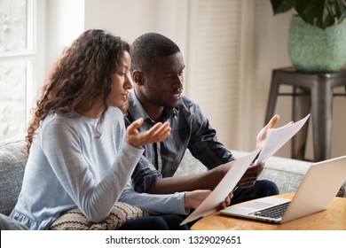 Concerned mixed race husband and wife take care of domestic bills reading papers at home, worried black couple consider bank documents, think of mortgage or loan, check paperwork together