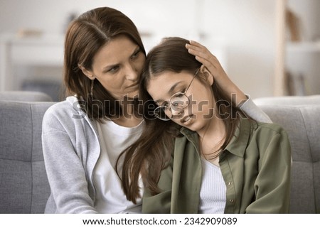 Concerned mother hugging upset teenager daughter child at home. Mom giving family support, empathy, comfort to teen girl in eye glasses sharing problems, failure, bad troubles