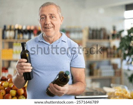 Concerned old man deciding between kinds of olive oil in the supermarket
