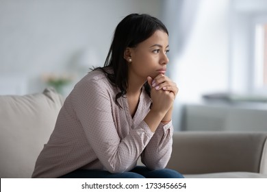 Concerned sad African woman sit on sofa in living room thinking of problem looks in distance feels depressed due loneliness, inner emptiness, life troubles, break up or divorce, marriage split concept - Powered by Shutterstock