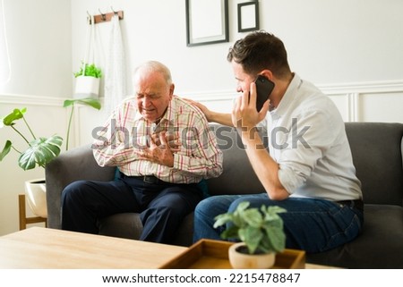 Concerned son calling emergency services on the phone because of his sick senior father having a heart attack