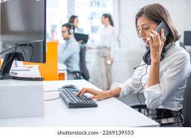 Concerned woman in business-wear talking on mobile phone, getting bad news and feeling depressed while working on computer at office. - Shutterstock ID 2269139553