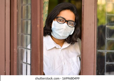 Concerned & worried lady under lock down home quarantine wearing protective breathing surgical face mask against flu and novel Corona virus (Covid-19) pandemic & greeting visitor through door/window - Powered by Shutterstock