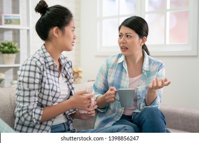 Concerned Young Girl Talking With Best Friend Sit On Couch Having Serious Conversation. Asian Chinese Woman Complaining Sharing Problems Or Concern. Sister Help Dealing With Depression Hold Cup.