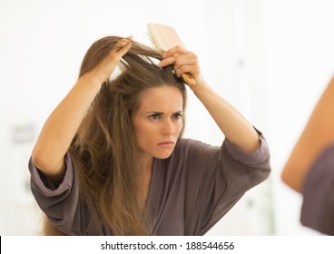 Concerned Young Woman Combing Hair In Bathroom