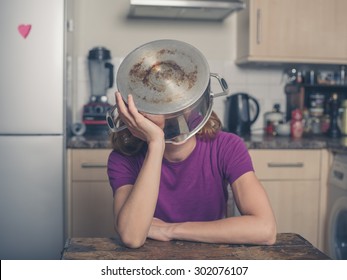 A concerned young woman is sitting at a table in a kitchen with a pot on her head